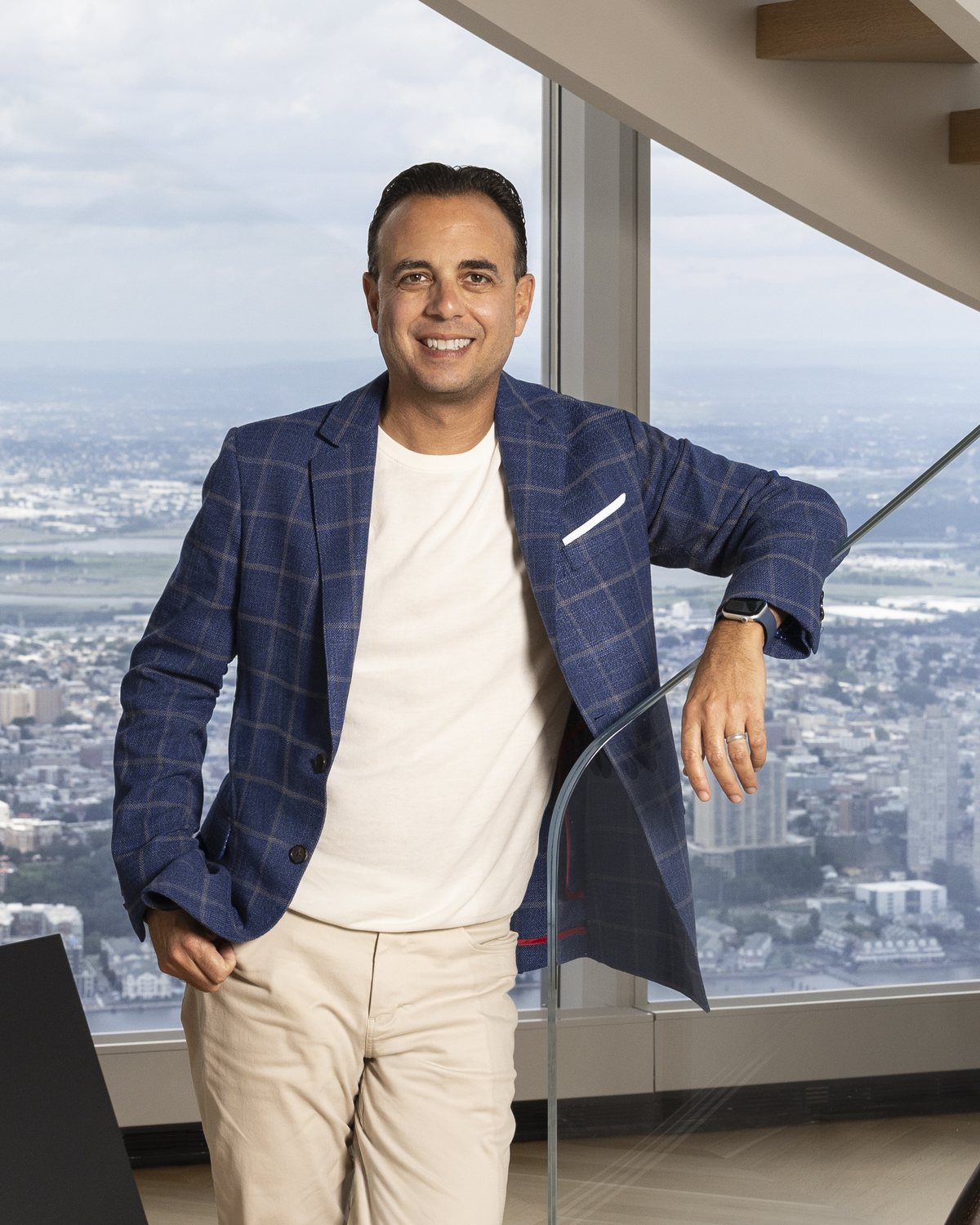 Jason Haber leaning on a glass stair rail in a high-rise with a city view behind him